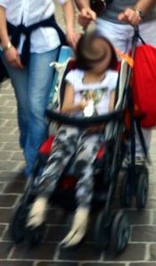 Bambina di almeno 4 anni (forse 5?) in passeggino; con questo gesto, i genitori le stanno comunicando: "Sei soltanto una bambina di un anno."
